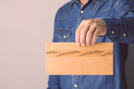 Businessman holding brown confidential envelope sealed with tape and word Please do not accept if seal is broken in Thai and English.の写真素材