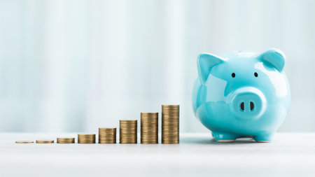 A blue piggy bank and stack of coins are neatly arranged on a table against a bright white...