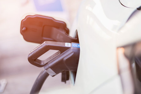 Concepts about using electric cars. An electric car user is holding a black charger to recharge an...