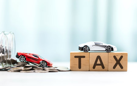 TAX is written on a wooden block next to a car model and a jar filled with coins and a small plant on a wooden table. Car tax awareness, financial planning, savings, and responsible money managementの写真素材