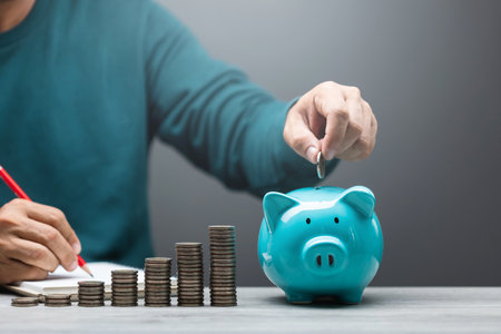 Man is dropping coins into a blue piggy bank, symbolizing the act of saving and financial...