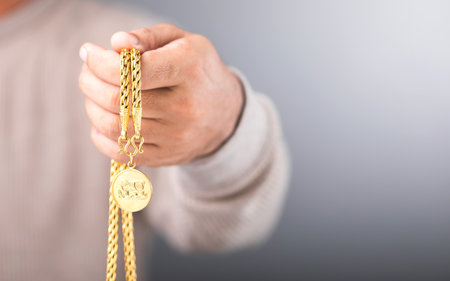Close-up of a man holding a gold necklace in his hand, symbolizing the concept of gold market value. Reflects checking the authenticity of the gold, exploring whether it's genuine or counterfeitの写真素材