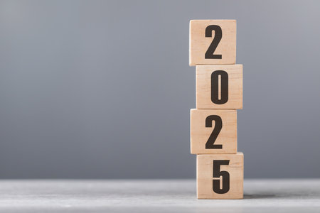 2025 is written on a wooden block placed on wooden table against a soft grey background. The image...