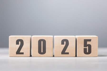 2025 is written on a wooden block placed on wooden table against a soft grey background. The image...