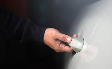 Man's hand reaching to open a car door. The image represents the concept of vehicle usage,...