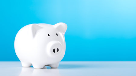 White piggy bank sits on a wooden table against a blue background, with ample copy space for text. The image symbolizes savings, financial planning, and responsible money management.の写真素材