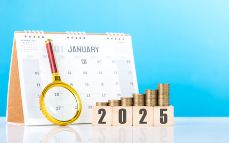 A stack of coins, a wooden block labeled '2025,' a magnifying glass, and a 2025 calendar. Financial goals and planning for the upcoming year, emphasizing careful budgeting and investment strategiesの写真素材