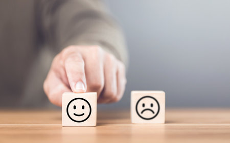 Man choosing between a happy and sad face on wooden blocks, ultimately selecting the happy one. The concept of starting each day with positivity, emphasizing the importance of a bright outlookの写真素材
