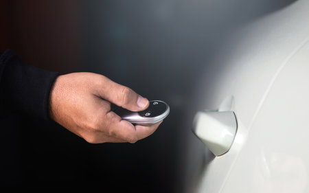 Man's hand holding a car remote to unlock the vehicle. The image represents the concept of using a...