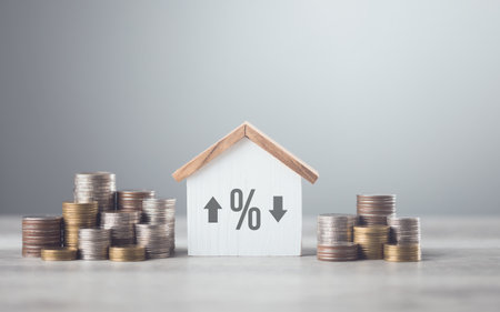 Stacks of coins arranged from smallest to largest, alongside a wooden house model on a table against a grey background. Concept of saving money for future investments, particularly in real estateの写真素材
