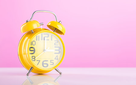 Yellow analog clock placed on a table against a pink background with ample blank space. The image emphasizes time management or scheduling, offering room for additional design or text elementsの写真素材