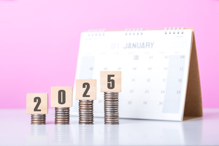 Stack of coins beside a wooden block labeled '2025' and a calendar. Symbolizes financial planning for the upcoming year, emphasizing budgeting and setting future investment goalsの写真素材