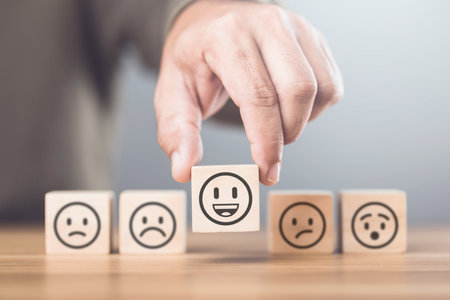 Man choosing between a happy and sad face on wooden blocks, ultimately selecting the happy one. The concept of starting each day with positivity, emphasizing the importance of a bright outlookの写真素材