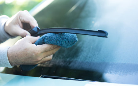 A car owner cleans the windshield wipers with a cloth, highlighting the importance of regular maintenance for optimal performance and clear visibility in all weather conditionsの写真素材