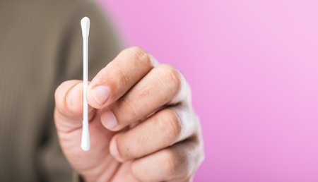 Close-up of a person holding a cotton swab against a pink background, highlighting the importance of correct usage and the recommendation to avoid reusing cotton swabs for hygieneの写真素材