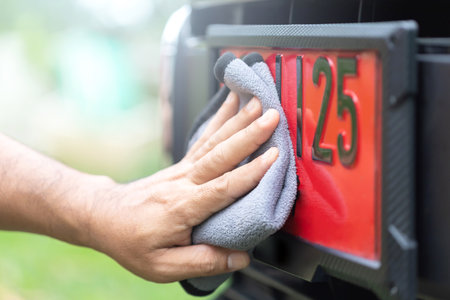 A car owner carefully cleans a red license plate, used for new cars before registration, reflecting Thai beliefs in lucky numbers and the importance of maintaining auspicious symbols for good fortuneの写真素材