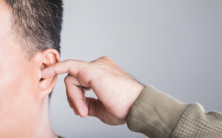 A close-up of a man using his finger to scratch inside his ear, highlighting the risks of ear irritation and injury from ear picking. This image emphasizes the importance of safe ear care practicesの写真素材