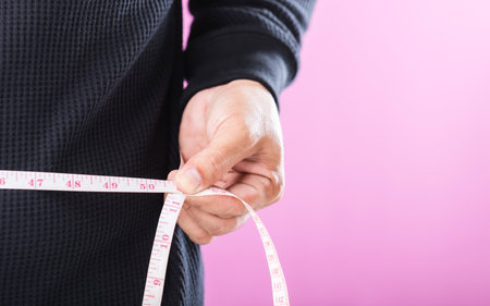A man measuring his waistline with a tape measure, emphasizing the importance of regular health...