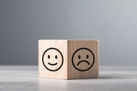 Wooden blocks displaying a sad face transitioning to a happy face, symbolizing a shift from negativity to positivity. Final block turns from sad to happy, highlighting the power of a positive outlookの写真素材