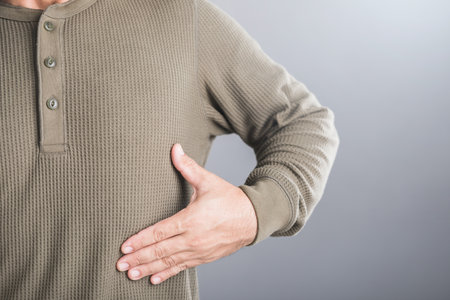 Man touches his left ribcage, showing signs of pain that may stem from rib muscle or cartilage inflammation. Discomfort associated with rib-related issues and the importance of musculoskeletal healthの写真素材