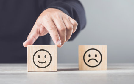 Man choosing between a happy and sad face on wooden blocks, ultimately selecting the happy one. The concept of starting each day with positivity, emphasizing the importance of a bright outlookの写真素材