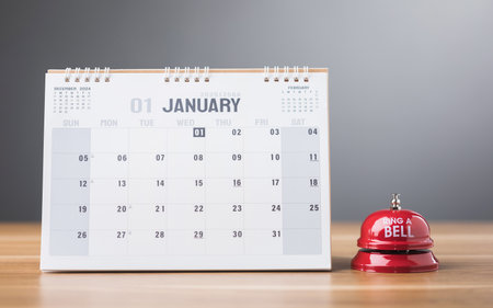 A 2025 calendar open to January with a red bell on the table, symbolizing fresh beginnings and the ringing in of the New Year. This image reflects the excitement of starting a new chapterの写真素材
