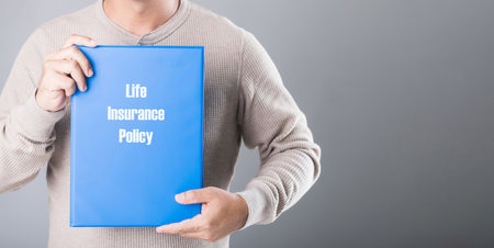 Man holds a blue life insurance policy booklet against a gray background, symbolizing the importance of planning and securing financial protection for the futureの写真素材