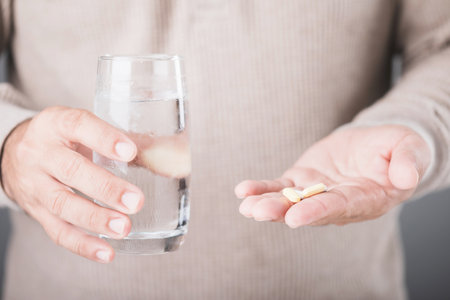 A man holding a glass of cold water and a pill, illustrating the common misconception of taking medication with cold water. Highlights the potential risks and importance of proper medication practicesの写真素材