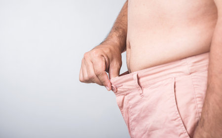 A man with a larger physique stands adjusting the waistband of his pants to check if they are tight...