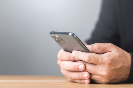A man types on his smartphone, engaged in a private online chat. The close-up view highlights the discreet nature of the conversation, reflecting secrecy and modern communicationの写真素材