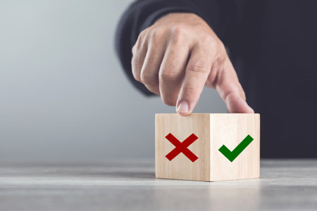 Man choosing between a checkmark and an 'X' symbol on wooden blocks. Image represents the concept of making the right choice, highlighting the importance of distinguishing between right and wrongの写真素材