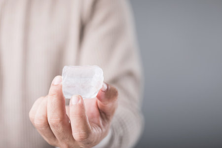 A man holding an ice cube, with a look of discomfort due to the cold, highlighting the sensitivity and potential tooth pain from consuming cold foods. Emphasizing oral health and dental careの写真素材