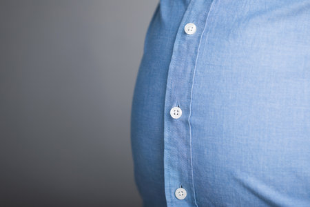An overweight person wearing a shirt that's too small, with visible tension on the fabric and gaps between the buttons, highlighting the struggle of improper fit due to body sizeの写真素材