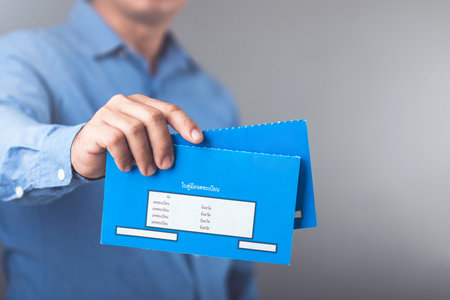 A businessman holds Thailand's blue vehicle registration book, issued after full loan repayment, symbolizing its use as collateral for loans or credit applications in Thailandの写真素材