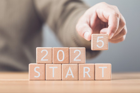 A businessman arranges wooden blocks spelling out 'START 2025' on a table, symbolizing the beginning of new goals and ventures for the upcoming year. Image reflects motivation and forward planningの写真素材