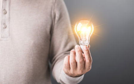 Man holds a clear light bulb, symbolizing the spark of new ideas and creativity. This image represents innovation, inspiration, and the power of fresh thinkingの写真素材
