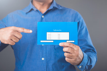 A businessman holds Thailand's blue vehicle registration book, issued after full loan repayment, symbolizing its use as collateral for loans or credit applications in Thailandの写真素材