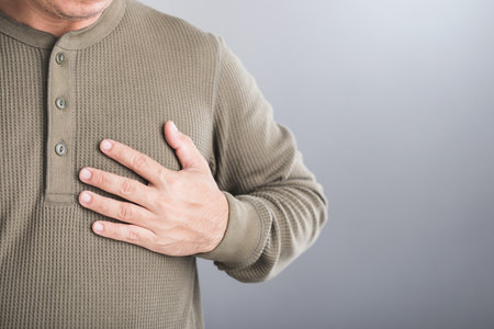 A man touches his left chest, indicating pain that may signal heart or cardiovascular issues. Image emphasizes the importance of early detection and awareness in preventing heart-related health risksの写真素材
