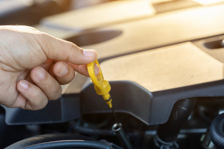 A car owner pulls out the dipstick to check engine oil levels, highlighting the importance of regular oil maintenance for optimal engine performance and vehicle longevityの写真素材