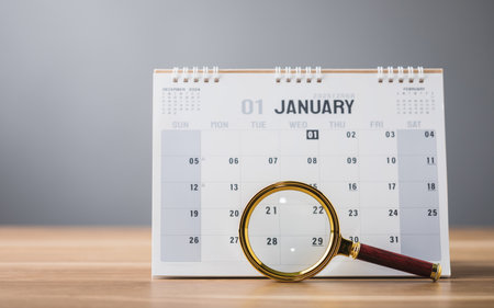 A 2025 calendar open to January with a magnifying glass on the table, symbolizing a closer look at new goals and plans for the year ahead. This image reflects a fresh start with focus and intentionの写真素材