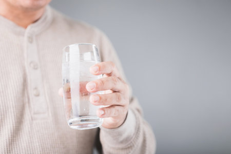 A man holding a glass of cold water with ice, showing a slight grimace due to tooth sensitivity. Image reflects the discomfort of consuming cold foods or drinks, highlighting dental health concernsの写真素材