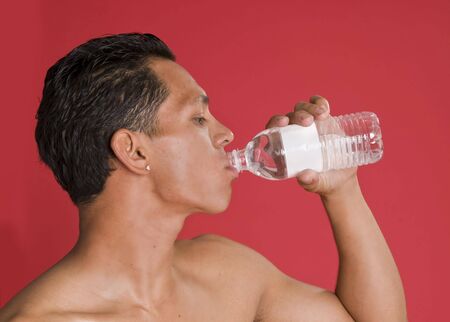 Attractive young man drinking bottle of water against red wall backgroundの写真素材