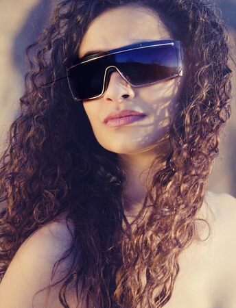 Beautiful young woman with gorgeous curly hair wearing sunglasses の写真素材