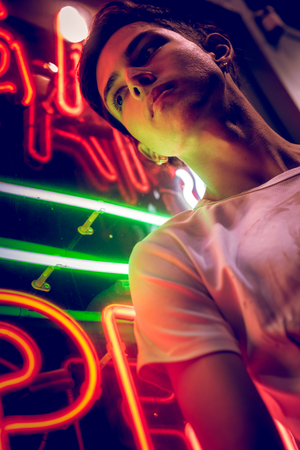 Young man lit by neon city street lights at nightの写真素材