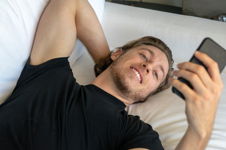 Smiling man looking at mobile cell phone while texting or face timing during call