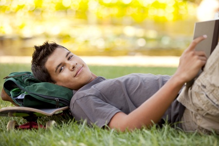 Student with skateboard and backpack reading in the grassの写真素材