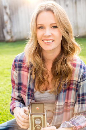 Young woman using her antique camera outside in the grassの写真素材