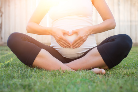 Pregnant woman outside holding her tummy with heart shaped hands