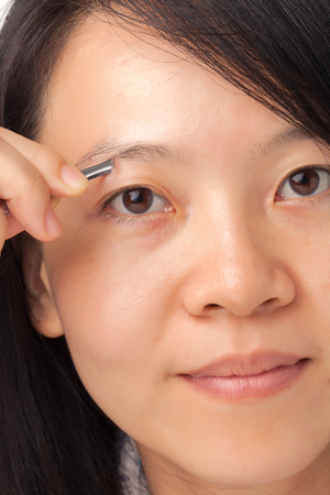 Woman plucking her eyebrows with tweezersの写真素材