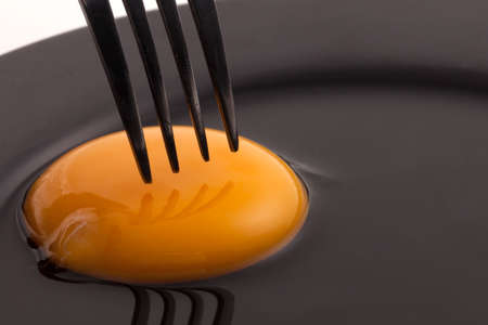 Egg closeup yolk with fork on black plateの写真素材